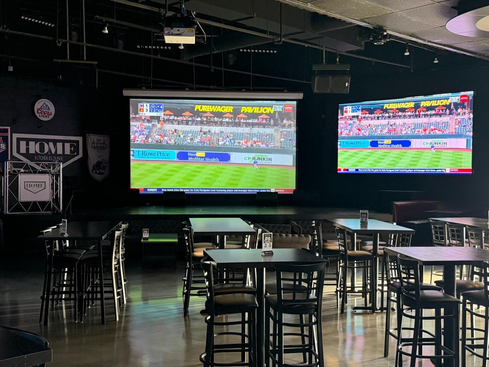 The projector screen and wall TVs showing a Cubs game