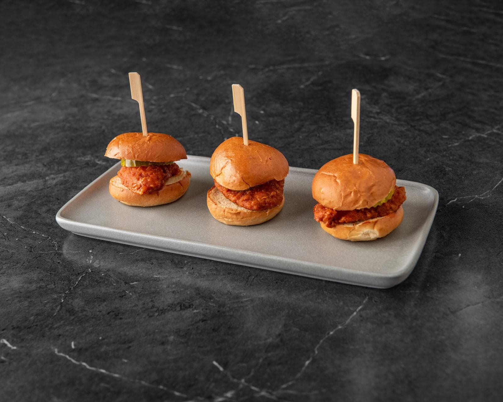 Three fried chicken sliders on a tray with pickles