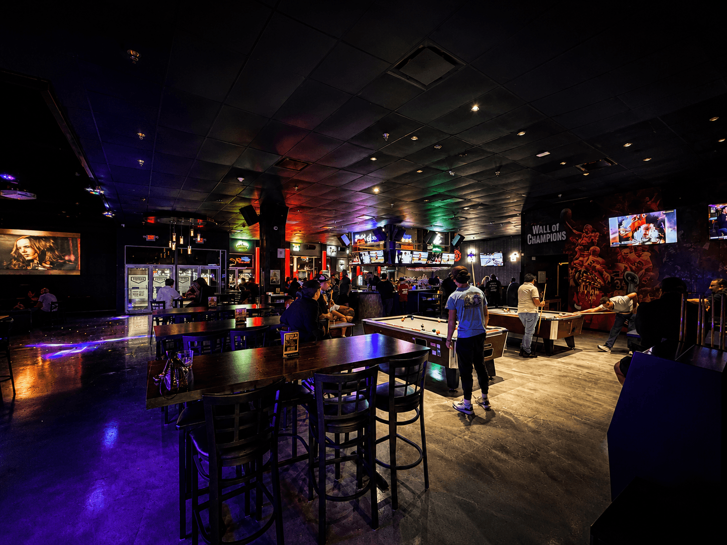The main floor at HOME — high-top tables and pool tables under coloured ceiling lights