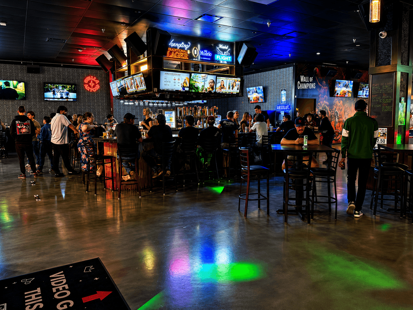 Guests gathered at the bar counter under neon lighting inside HOME Sports Bar