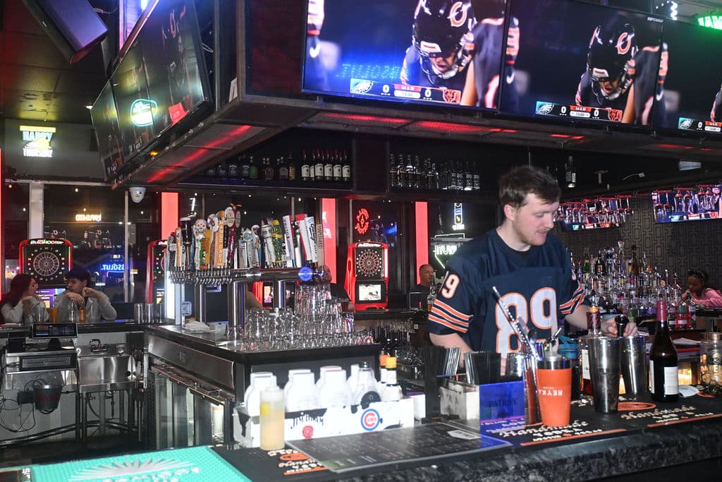Bartender in a Bears jersey working the bar under the big screens